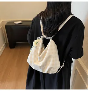 Détail du sac bandoulière à carreaux avec breloque lune en peluche et logo en cuir