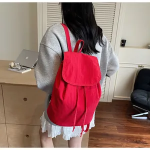 Rear view of a red drawstring backpack with flap closure on a model in minimalist interior