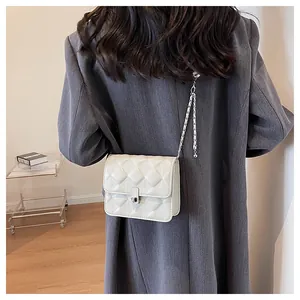 Detail of cream quilted chain bag worn over the shoulder showing silver lock and texture