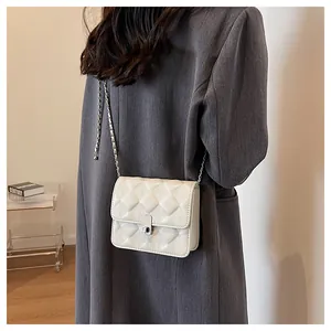 Detail of white quilted crossbody bag with silver chain strap and metal clasp on shoulder