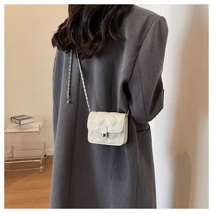 Detail of white quilted mini bag with silver twist lock and chain strap on grey blazer