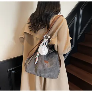 Detail of grey canvas tote bag with brown leather straps and colorful beaded pendants