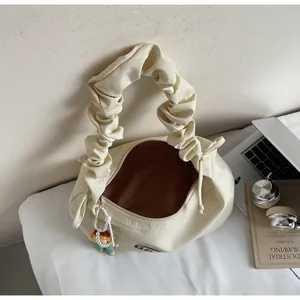Close-up of a cream-colored pleated handbag featuring a cute cartoon charm and drawstring