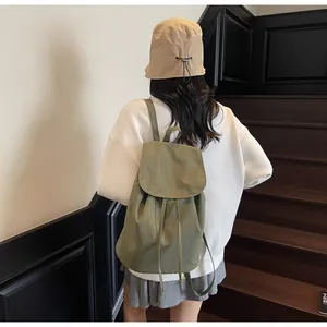 Detailed back view of a sage green drawstring backpack worn by a model on stairs