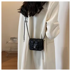 Detail of black quilted crossbody bag with silver clasp and metal chain on white blazer