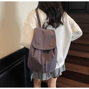 Detail of a deep purple drawstring backpack in nylon shown on a model's back in a minimalist setting