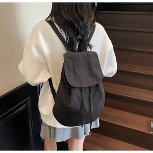 Minimalist black canvas drawstring backpack shown on a model standing on wooden stairs