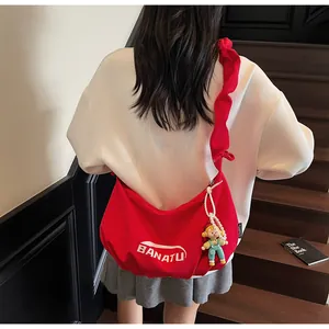 Red crossbody bag with pleated strap and cute doll pendant worn by model outdoors