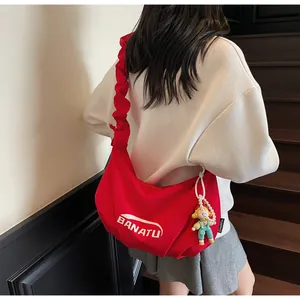 Detail of red canvas tote with ruched strap and cute pearl doll charm on shoulder bag