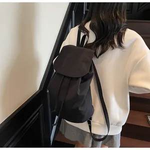 Rear view of model wearing a minimalist black drawstring backpack on a wooden staircase