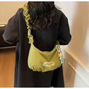 Green crescent crossbody bag with ruched strap and doll charm on a female model
