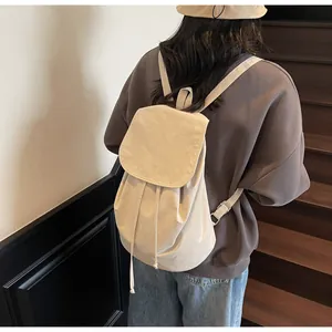Detailed back view of a beige drawstring backpack worn by a model in a minimalist stairwell