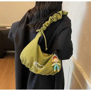 Detail of avocado green crossbody bag featuring ruched cloud strap and cute doll pendant