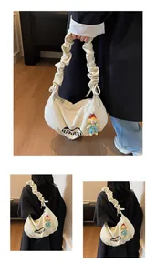 Detail of white crescent canvas bag with pleated strap and cute doll pendant accessory
