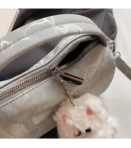 Detalle de cremallera plateada y colgante de gato de peluche en bolso Boston gris
