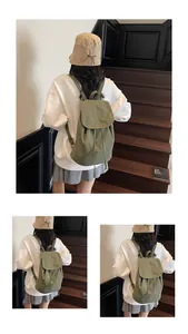 Army green drawstring backpack in canvas material worn by a model on wooden stairs