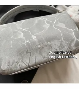 Detalle de bolso Boston gris con textura de ondas y colgante de bola de peluche en el asa