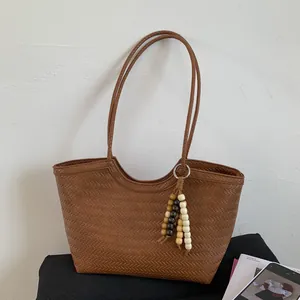 Gros plan d'un sac cabas tressé marron orné d'un gland décoratif en perles sur le côté