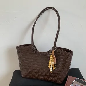 Vue détaillée du sac cabas tressé marron foncé avec pompon en perles et motifs texturés