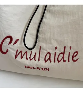Close-up of red cursive embroidery on white lightweight crinkled fabric shoulder bag
