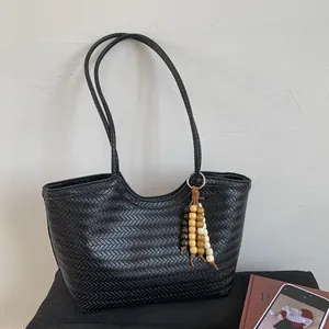 Détail du cabas tressé noir avec texture en V et pompon en perles de bois colorées