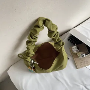 Avocado green pleated handbag with cloud handle and beaded charm on white bedding