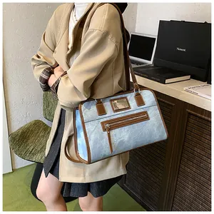 Close-up of light blue denim shoulder bag with brown leather trim and metal logo