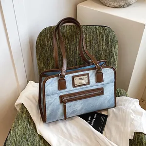 Large blue denim tote bag with brown leather trim and metal logo on a woven chair
