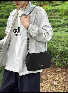 Outdoor shot of a black nylon crossbody bag with woven strap and branding detail