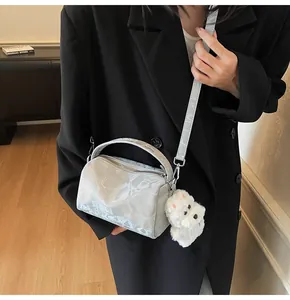 Detalle de bolso Boston plateado con textura metálica y colgante de perrito de peluche