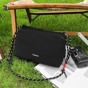 Sporty black nylon crossbody bag with woven rope strap on outdoor grass background