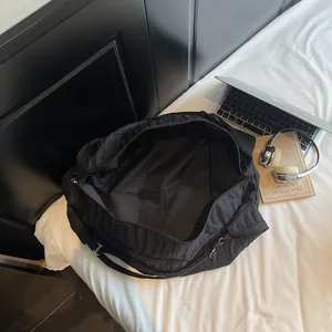 Large capacity black nylon tote bag shown with daily essentials on a white bed