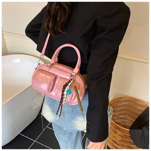 Pink patent leather baguette bag featuring front pockets and woven decorative charms
