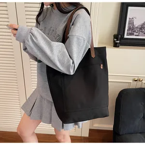Close-up of black canvas tote bag showing large front pocket and brown leather handles