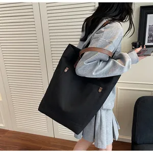 Detail view of black canvas tote bag featuring brown leather straps and metal buckle accent