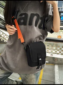 Detail einer schwarzen Umhängetasche aus Nylon mit leuchtend orangem breitem Schultergurt