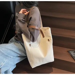 Detail of canvas tote bag with brown leather strap and front pocket accent
