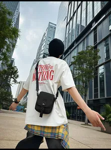 Street-Style-Ansicht einer schwarzen Umhängetasche mit weißem Grafik-T-Shirt und Karohemd