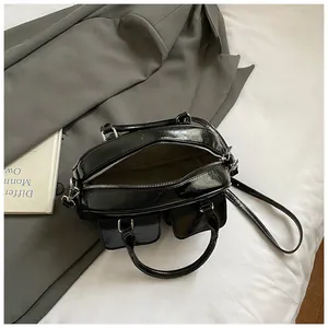 Glossy black baguette shoulder bag with dual front pockets and silver zipper detail