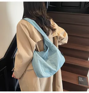 Detail of light blue hobo bag with black brand label worn with a khaki trench coat