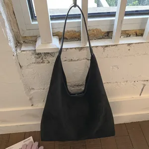 Macro detail of black suede shoulder bag with minimalist hobo silhouette and strap
