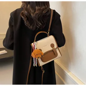 Detail of a chic cream and brown contrast shoulder bag with a cute plush bear charm