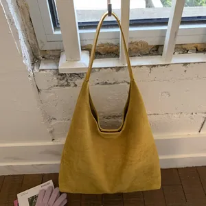Detail of a large yellow suede tote bag hanging on a rustic white brick wall