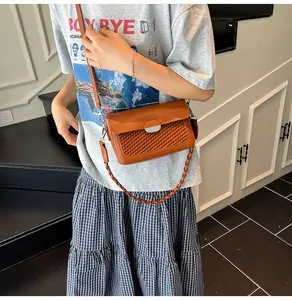 Detail of brown crossbody bag with woven texture lid and dual straps shown on model