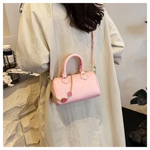 Detail of pink Boston bag with strawberry charm worn by model in a cozy indoor setting