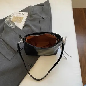 Minimalist black leather shoulder bag with silver pendant on casual grey blazer background