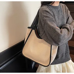 Gros plan d'un sac cabas en toile beige avec garniture en cuir noir porté à l'épaule