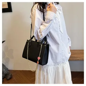 Gros plan du sac à main noir avec pendentif fraise rouge et bandoulière en chaîne dorée