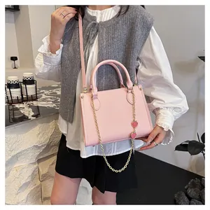 Détail du sac à bandoulière rose clair avec chaîne dorée et breloques cœur rouge sur cuir