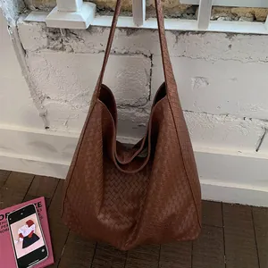 Retro large brown woven leather tote bag hanging on a white brick wall for daily wear